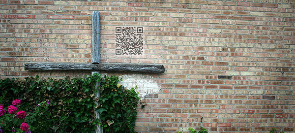 Cross in a garden with QR code on brick wall