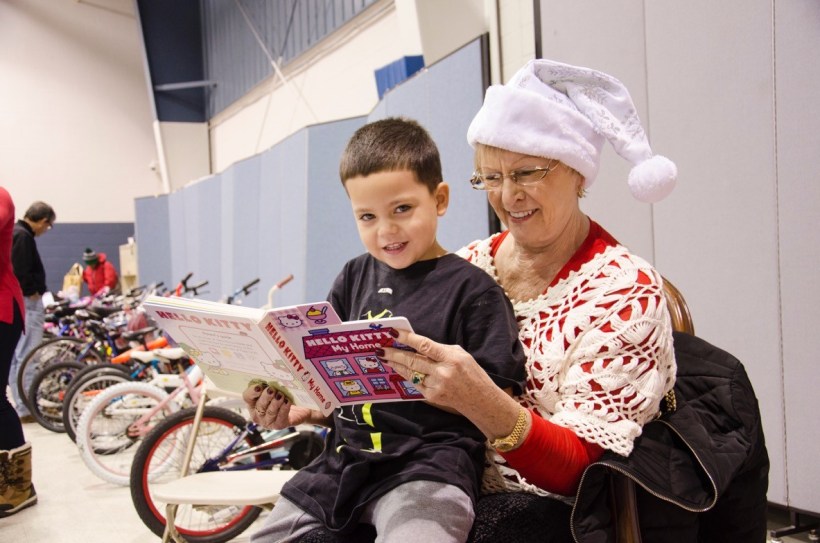 Child sitting on Santa helper's lap with book