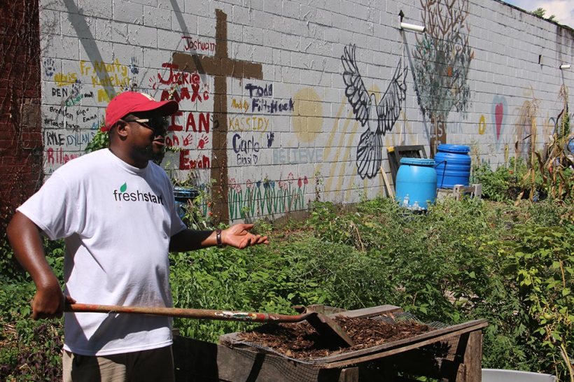 In front of building wall painted with cross and encouragement Justice Slappy speaking, while raking 
