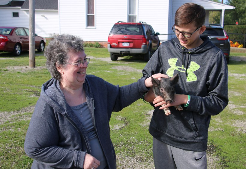 Pastor pets piglet held by a teen boy